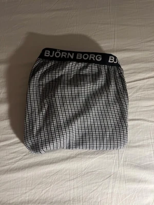 Rutig Björn Borg mjukisbyxa - Säljer ett par mjukisbyxor från Björn Borg med svartvitt rutigt mönster och bred resår med logga i midjan. Byxorna är långa och har en avslappnad passform, perfekta för chill dagar hemma. Tillverkade i mjukt material för extra komfort.