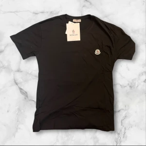 Svart t-shirt från Moncler - Säljer en svart t-shirt från Moncler med klassisk rund hals och korta ärmar. T-shirten har en liten Moncler-logga broderad på bröstet och är gjord i mjuk bomull. Perfekt för dig som gillar stilrena och enkla plagg med exklusiv känsla.