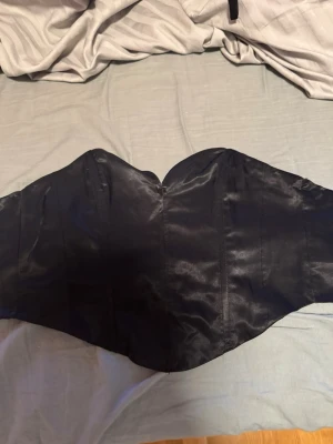 Svart satin korsett med dragkedja - Säljer en svart korsett i glansigt satinmaterial. Modellen är axelbandslös med en snygg sweetheart-ringning och dragkedja i sidan för enkel på- och avtagning. Perfekt för att lyfta vilken outfit som helst. Perfekt nu till nyår!!💞