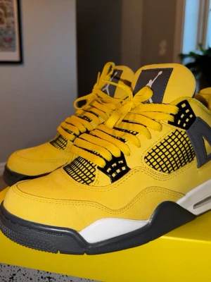 Nike Jordan 4 Retro 'Thunder' sneakers - Säljer ett par Nike Jordan 4 Retro 'Thunder' sneakers i starkt gul mocka med svarta och grå detaljer. Skorna har snörning, platt sula och ikoniska meshpaneler på sidorna. Perfekt för dig som vill sticka ut med färg och streetstyle.