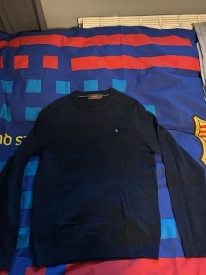 Blå merinoulltröja från Morris - Säljer en stilren mörkblå tröja från Morris i 100% merinoull. Tröjan har rund hals, lång ärm och en liten broderad logga på bröstet. Perfekt för dig som gillar klassisk och enkel design med en exklusiv känsla.