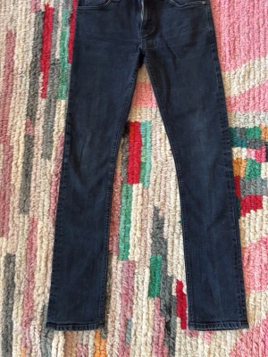 Svarta jeans från Nudie - Säljer ett par svarta skinny jeans från Nudie Jeans med klassisk femficksdesign och snygga detaljer på bakfickan. Jeansen har dragkedja och knapp framtill, och är gjorda i mjukt jeansmaterial som sitter tight och bekvämt. Pris kan diskuteras.