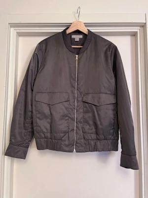 Sagegrön Bomberjacka i satin - Bomberjacka från H&M med klassisk rund krage och dragkedja framtill. Jackan har två stora fickor med lock och elastisk nederkant. Sage/Militär/Khakigrön. Yttermaterialet är i satin och innefoder i imitationsilke. Riktigt klassig med lyxig känsla. Storlek L för oversized look som jag använt över klänningar på sommaren, samtidigt som den är perfekt för vår och höst. Mucka bra skick, som ny! Säljs på flera sidor, först till kvarn. 