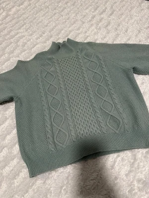 Grön stickad polotröja från Bubbleroom - Snygg grön stickad polotröja från Bubbleroom i storlek S. Tröjan har ett flätstickat mönster framtill och ribbade muddar vid hals, ärmslut och nederkant. Perfekt för dig som gillar mysiga och stilrena plagg med lite struktur.