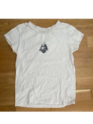 Brandy Melville tröja  - Vit t-shirt från brandy Melville med ett svart tryck av ett hjärta med törnekrona och eld på bröstet. Storlek S