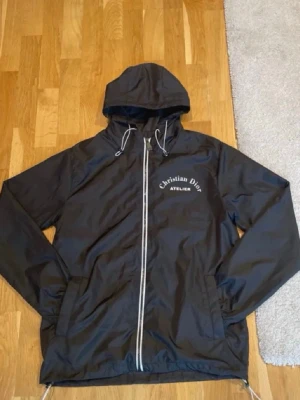 Svart Vindjacka - Hej! Säljer en windbreaker jacka som jag hittade när jag rensade i min brorsas gamla rum (han har flyttat ut). Jackan ser helt ny ut och verkar aldrig vara använd. Har inte så bra koll på märken, men tänkte att det är bättre att den kommer till användning än att den bara ligger.