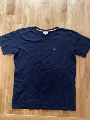 T-shirt Lacoste - Snygg mörkblå t-shirt från Lacoste med klassisk krokodillogga broderad på bröstet. Knappast använd samt inga defekter! 