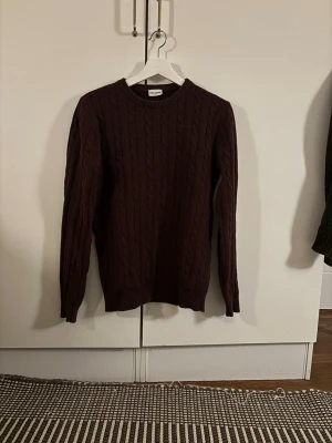Vinröd kabelstickad tröja John Henric - Snygg vinröd kabelstickad tröja från John Henric. Rund halsringning och ribbade muddar vid ärmslut och nederkant. Tröjan har ett klassiskt mönster och sitter bra på kroppen, perfekt till jeans eller chinos. Modellen i bilden är 180 och väger 72 kg