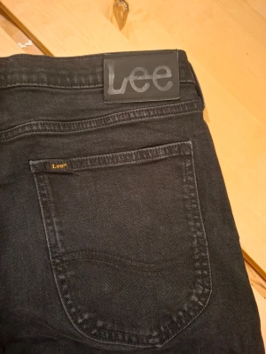Svarta Lee Luke jeans  - Svarta jeans från Lee, modell Luke, med klassisk femficksdesign och Lee-logga på bakfickan. Jeansen har en rak passform.  Perfekt för dig som gillar stilrena och tidlösa jeans. Priset är inte hugget i sten.