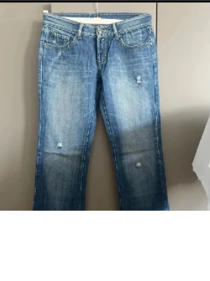 Blå jeans från Seven7 med gul detalj - Snygga blå jeans från Seven7 med gul broderad detalj på bakfickorna och slitningar framtill. Klassisk femficksmodell med knappstängning och gul logotyp på insidan. Jeansen har en rak passform och är tillverkade i jeansmaterial.