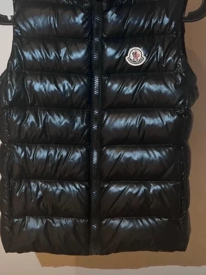 Svart dunväst från Moncler - Säljer en svart, glansig dunväst från Moncler med klassisk quiltad design och dragkedja framtill. Västen har Moncler-logga på bröstet och är tillverkad i syntetmaterial med dunfyllning. Perfekt för dig som vill ha en cool och varm look. En lapp har gått av inuti västen men inte man tänker på! Den är testad på monclears hemsida och är såklart äkta!