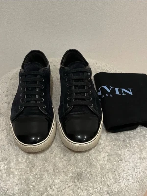 Lanvins  - Säljer ett par svarta sneakers från Lanvin i mjuk mocka med vita sulor och klassisk snörning. Skorna har en stilren och tidlös design som passar till många olika outfits. Medföljer originalpåse från Lanvin.