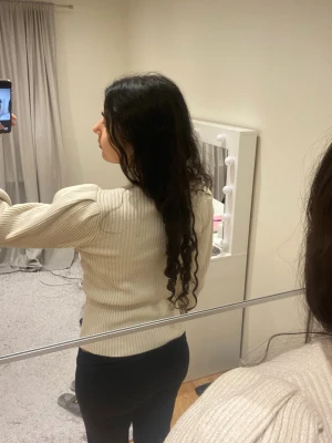 Beige ribbad stickad tröja - Säljer en beige ribbad stickad tröja med hög hals och puffiga ärmar. Tröjan har en slim passform och är superenkel att matcha med olika outfits. Perfekt för dig som gillar en stilren och trendig look.