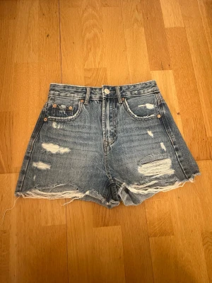 Jeansshorts från Stradivarius - Snygga blå högmidjade jeansshorts från Stradivarius med slitna detaljer och fransig kant nertill. Klassisk med knapp och dragkedja. Perfekta för en chill sommarlook.