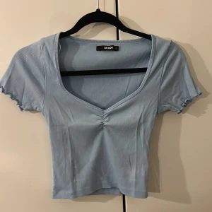 Ljusblå ribbad topp från Bik Bok - Säljer en ljusblå ribbad topp från Bik Bok i storlek S. Toppen har v-ringning med rynkdetalj framtill, korta ärmar med vågiga kanter och croppad passform. Perfekt för vår och sommar, superenkel att styla med jeans eller kjol.