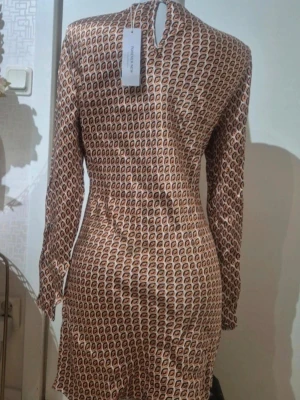 Mönstrad kortklänning från Forever New - Snygg kortklänning med lång ärm från Forever New. Klänningen har ett grafiskt mönster i orange, svart och vitt, rund hals,Materialet känns mjukt och lätt, perfekt för dig som gillar att sticka ut med coola prints. Storlek 42 🛍