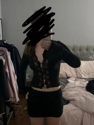 Svart långärmad topp med spetsdetaljer - Säljer en svart långärmad topp med snygga spetsdetaljer framtill och djup v-ringning. Toppen är croppad och har en tight passform som framhäver midjan. 