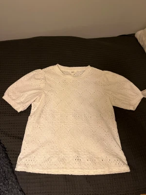 Vit spetsblus från Object - Säljer en söt vit blus från Object i storlek S. Blusen har korta puffärmar och är täckt av ett broderat spetsmönster med små hål för en luftig känsla. Perfekt till jeans eller kjol för en fräsch look.