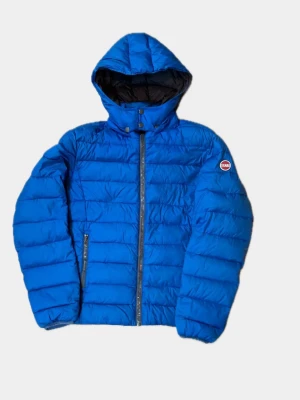 Blå pufferjacka från Colmar med huva - Säljer en blå pufferjacka från Colmar med huva och dragkedja framtill. Jackan har ett quiltat mönster och en snygg logga på ärmen. Perfekt för kalla dagar och har praktiska fickor med dragkedja. Passar dig som gillar sportig och clean stil.