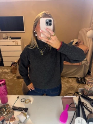 Mörkgrå stickad polotröja - Säljer en mörkgrå stickad polotröja med hög krage och långa ärmar. Tröjan har en loose passform och är perfekt för kyligare dagar. Enkel och stilren design som passar till jeans eller kjol.