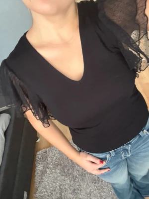 Svart topp med volangärmar - Säljer en svart topp med v-ringning och transparenta volangärmar i mesh. Toppen har en figurnära passform och är tillverkad i mjukt material. Perfekt till vardags och till festen🤩🥰 