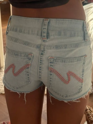 NELLY SHORTS💕 - Säljer ett par ljusblå fina shorts med rosa broderi på fickorna. De är från Nelly och är köpta som shorts.knappt andvända
