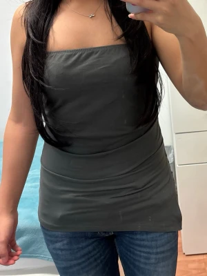 Mörkgrå tubtopp med slits - Säljer en enkel och stilren mörkgrå tubtopp i stretchigt material. Toppen är axelbandslös och har en lång passform med slits på sidan för en cool look. Perfekt att matcha med jeans eller kjol för en avslappnad vibe.