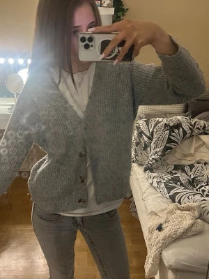 Grå stickad kofta från Zara - Mysig grå stickad kofta från Zara med v-ringning och tre knappar framtill. Koftan har en loose passform och är perfekt att slänga på sig över en t-shirt. Enkel och stilren design som funkar till det mesta.