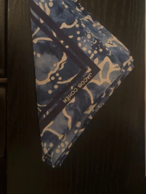 Blommig blå garment från Jacob Cohën - Säljer en snygg accessoar från Jacob Cohën med blått och vitt blommigt mönster. Tyg i sidenliknande material som känns lyxigt och mjukt. Perfekt för att addera lite färg och stil till din outfit.