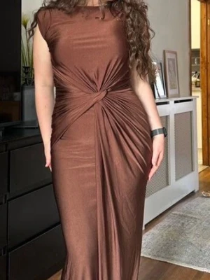 Brun långklänning med knutdetalj - Säljer en snygg brun långklänning i mjukt stretchigt material. Klänningen har korta ärmar och en unik knutdetalj i midjan som ger en cool draperad effekt. Perfekt för dig som gillar stilrena plagg med twist. Ingen synlig logga eller märke.