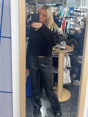 Svarta byxor i skinnimitation - Säljer ett par svarta byxor i skinnimitation med rak passform. Byxorna har normal passform, hällor för bälte och klassisk femficksdesign. Perfekta för dig som vill ha en edgy och trendig look.