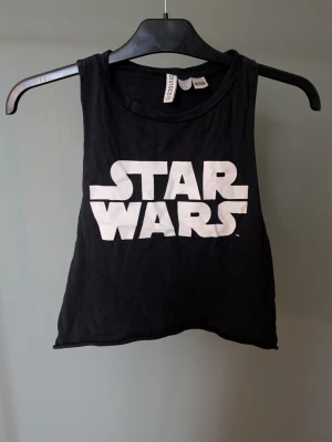 Svart Star Wars linne - Cool svart linnetopp från H&M Divided med stort vitt Star Wars-tryck på framsidan. Toppen är ärmlös och croppad, perfekt till jeans eller shorts. Tillverkad i mjuk bomull som känns skön mot huden.