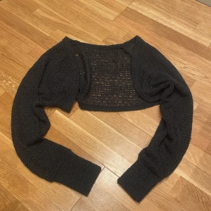 Svart stickad bolero från DAZY XS - Säljer en svart, stickad bolero från DAZY i storlek XS. Tröjan är virkad med ett genombrutet mönster och har långa ärmar med breda muddar. Perfekt att slänga över ett linne eller klänning.