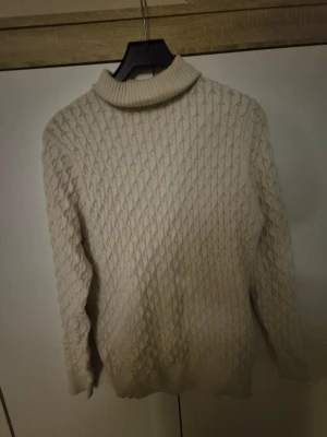 Beige polotröja från Approach S - Säljer en beige polotröja från Approach i storlek S. Tröjan har ett snyggt kabelstickat mönster, ribbad polokrage och långa ärmar. Perfekt för kyliga dagar och enkel att matcha med jeans.