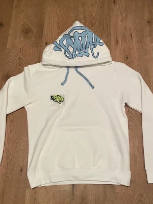 Syna world hoodie - Säljer en vit syna world hoodie med blå snören och blå logga på huvan. Storlek S