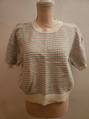 Randig stickad topp från & Other Stories - Säljer en söt stickad topp från & Other Stories i storlek L. Tröjan har korta ärmar, rund halsringning med vågig kant och ett randigt mönster i pastellfärger: ljusgrön, ljuslila och beige. Perfekt för vår och sommar när du vill ha något bekvämt men ändå stilrent.