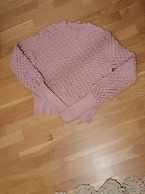 Rosa stickad tröja från Lindex  - Supersöt rosa stickad tröja från Lindex i storlek XS. Tröjan har ett unikt strukturmönster som påminner om fjäll och breda muddar vid ärmslut och nederkant. Perfekt för dig som vill ha något mysigt och snyggt till hösten eller vintern.