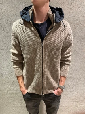 Massimo dutti cardigan  - Säljer en beige stickad overshirt med dragkedja och avtagbar mörkblå huva. Jackan har en grovstickad struktur, ribbade muddar och en avslappnad passform. Perfekt för lager på lager och chill stil.