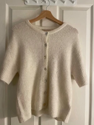 söt kofta - Stickad kortärmad kofta/topp i mjuk, krämvit färg med knappar framtill. Superfin både öppen och stängd. I väldigt fint skick och sparsamt använd. Perfekt basplagg som passar året runt 