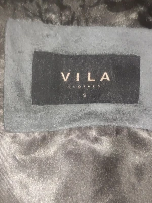 Grå pälsväst med bälte från Vila - Säljer en snygg grå pälsväst från Vila i storlek S. Västen har ett mjukt pälsmaterial och ett matchande bälte som knyts i midjan för extra stilpoäng. Perfekt att slänga över en hoodie eller långärmad tröja för en cool look.