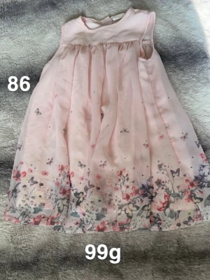 Ljusrosa blommig klänning 86 - Söt ljusrosa klänning med ärmlös design och blommigt mönster samt små fjärilar nertill. Klänningen har ett lätt och luftigt tyg som ger ett fint fall. Perfekt för varma dagar och speciella tillfällen.🌸 Fint använt skick. Storlek 86