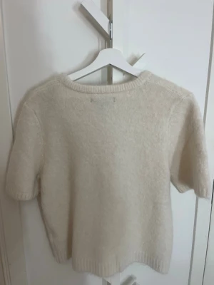 Beige stickad tröja från Amisu - Mysig beige stickad tröja från Amisu med korta ärmar och rund hals. Tröjan har ribbade kanter vid ärmslut och nederkant, perfekt för lager på lager under höst och vår. Enkel och stilren design som passar till det mesta. Pris går att diskutera.