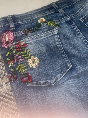 Vintage jeans med broderade blommor - Jättesnygga jeans med broderade blommor och symboler både fram och bak. Storleken är M men skulle säga XS-S, är själv XS och dom är lite baggy på mig men passar runt höfterna. Vet dock inte om dom passar på Medium! Jag är 150cm och byxorna är bara lite för långa. (PRIS KAN DISKUTERAS OCH KNAPPEN ÄR LITE LÖS).