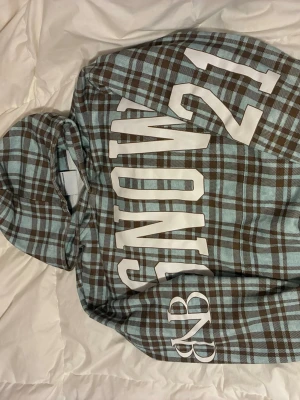 Snow Strippers 2026 Merch - Farmers Daughter Plaid Hoodie från deras 2025-2026 EU tour. 