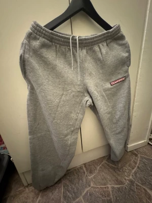 Grå mjukisbyxor från Team Sportia - Säljer ett par grå mjukisbyxor från Team Sportia i storlek S. De har elastisk midja med snörning och en broderad logga på vänster ben. Perfekta för chill eller träning, tillverkade i mjukt bomullsmaterial för extra komfort.