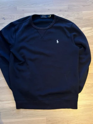 Mörkblå sweatshirt från Polo Ralph Lauren - Snygg mörkblå sweatshirt från Polo Ralph Lauren i storlek M. Tröjan har rund halsringning, lång ärm och klassisk broderad logga på bröstet. Tillverkad i mjuk bomull som är skön att ha på sig. Perfekt för chill dagar och enkel att matcha med jeans eller joggers.