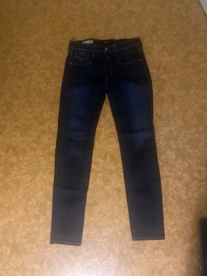 Replay Anbass mörkblå jeans strl 31 -  Snygga Replay Anbass jeans i mörkblå tvätt med klassisk femficksdesign och kontrastsömmar. Modellen är slim och har raka ben med smal passform. Materialet är stretchigt jeans för extra komfort. Bakfickorna har coola broderade detaljer. 31/32