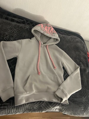 Syna world - Säljer ett par grå mjukisbyxor med rosa graffiti-tryck baktill och broderad text 'Forgive Me' vid benet. Byxorna har resår i midjan och dragkedja vid benslut. Tillverkade i mjukt material, perfekta för chill dagar.