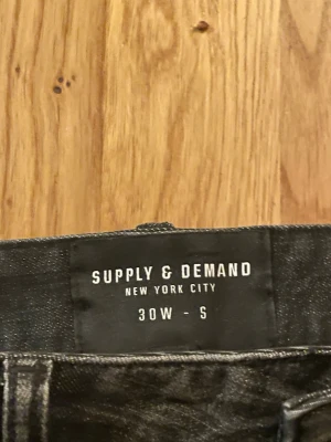 Svarta jeans från Supply & Demand - Svarta jeans från Supply & Demand med coola slitningar och vita färgstänk på benen. Skinny fit och klassisk femficksdesign. Perfekt för dig som gillar streetstyle och vill sticka ut med en edgy look.