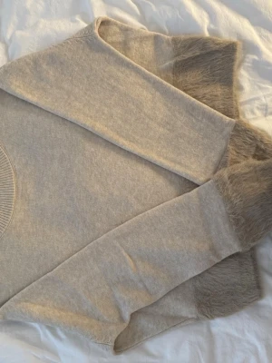 Beige stickad tröja med pälsdetaljer - Säljer en beige stickad tröja med fluffiga pälsdetaljer vid ärmsluten och nederkanten. Perfekt för kalla dagar när du vill vara både varm och snygg.